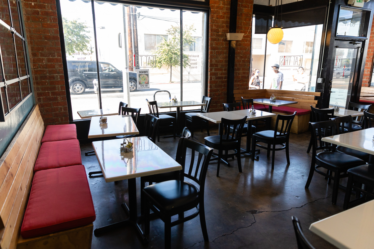 Sunlit Eat This Café dining room in Hollywood with exposed brick walls, wooden banquettes and tall storefront windows