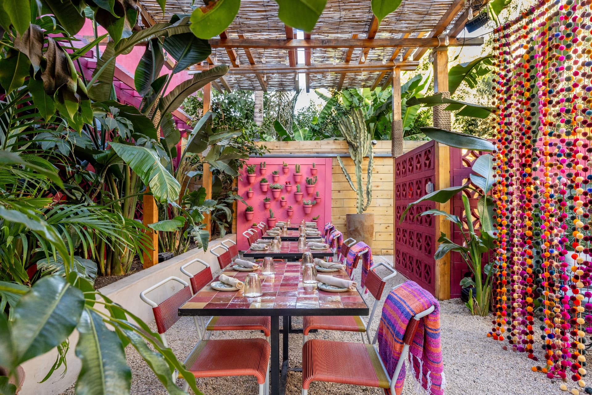 Isla Rosa at Tacolina with pink tiled tables and lush greenery beneath a shaded canopy